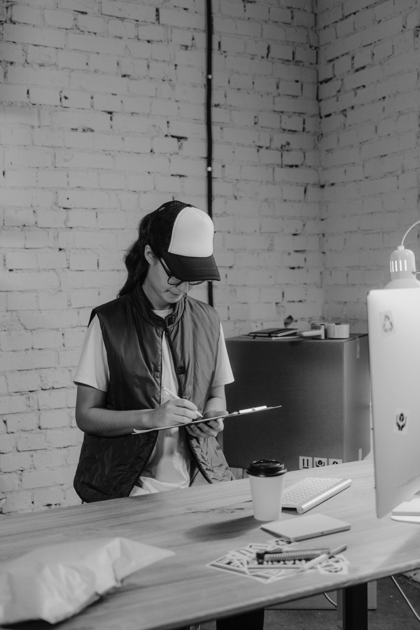 Black-and-white image of a female warehouse worker writing on a clipboard in an office setting.